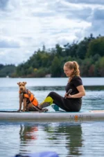Persoon peddelt met Moai 10'6 SUP‑board en hond op het water